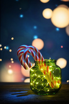 Small green jar with twinkle lights and candy canes with whimsical background