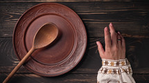 Ukrainian woman sitting in national restaurant and waiting for order. Girl knocks fingers nervously on wooden table while waiting for dish. Empty clay plate with spoon.