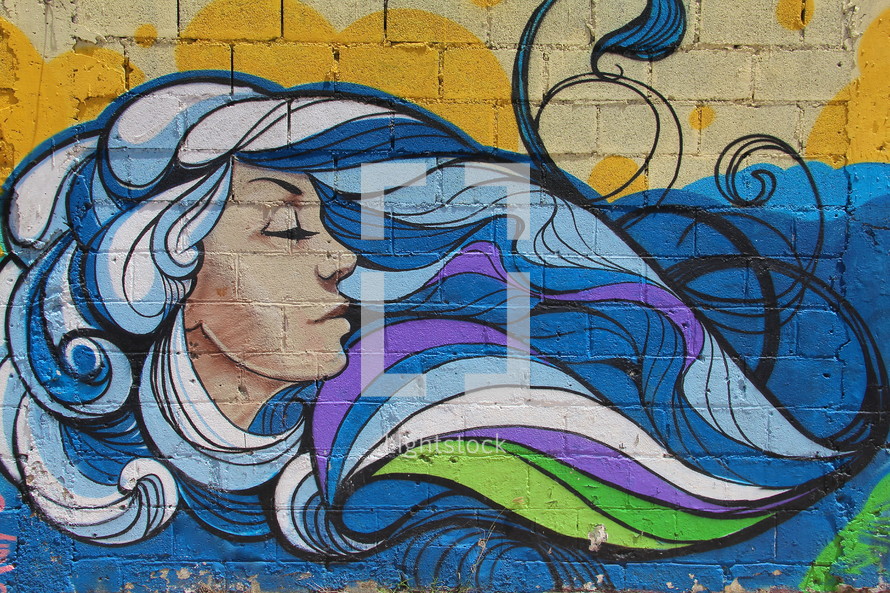 Graffiti painting of a woman with flowing wavy blue hair on a brick wall background 