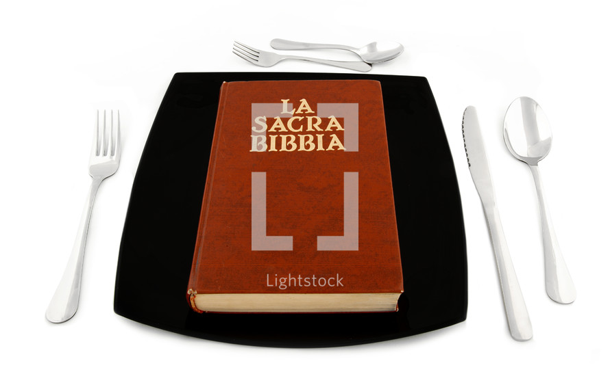 Metaphoric concept with bible in the plate with cutlery on white table.