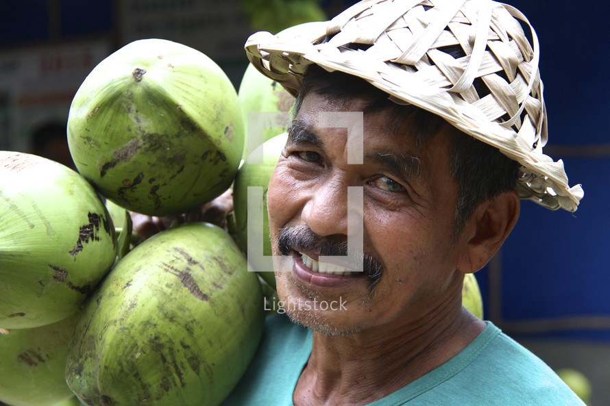 a smiling man in a coconut frond hat holding a bunch of coconuts