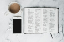 opened Bible, earbuds, smartphone, and coffee mug 