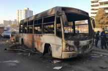 Burnt remains of a bus with emergency responders in background