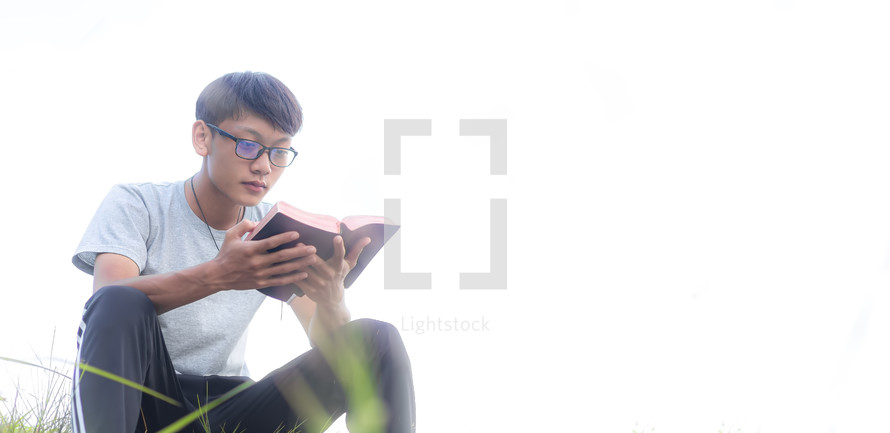 a young man reading a Bible outdoors 