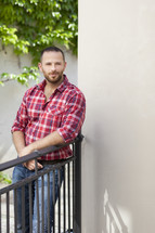a man in a plaid shirt leaning against a fence 
