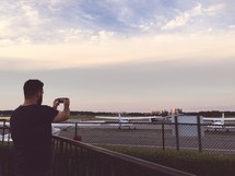 a man taking a picture of planes at an airport runway 