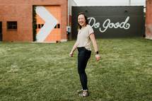 a smiling young woman in front of a do good sign 