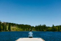a man sitting at the end of a pier over a lake 
