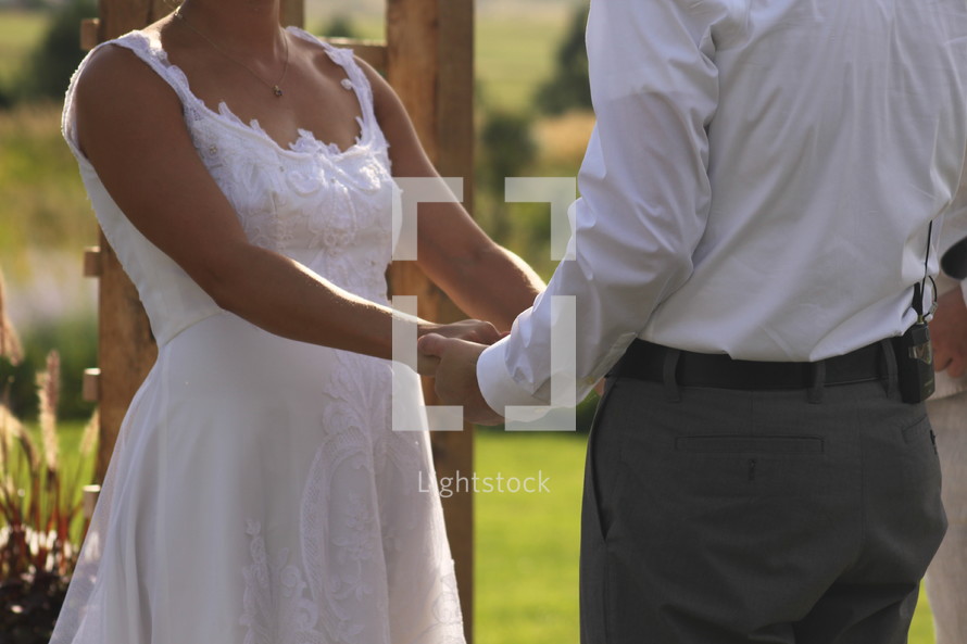 torso of a bride and groom holding hands 