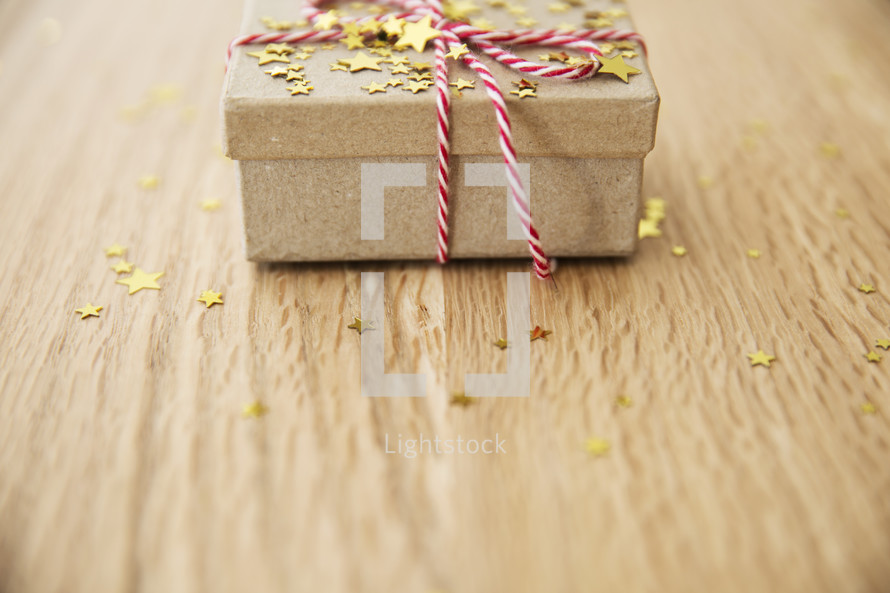 star confetti and red and white string around a brown paper gift box 