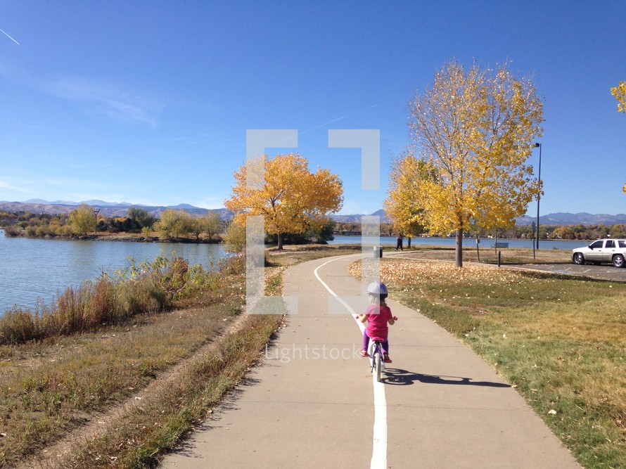 a toddler girl riding a bike along a trail 