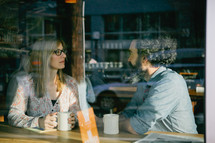 Window view of a couple having coffee.