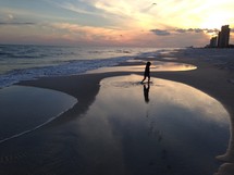 a little girl walking on a beach at sunset 