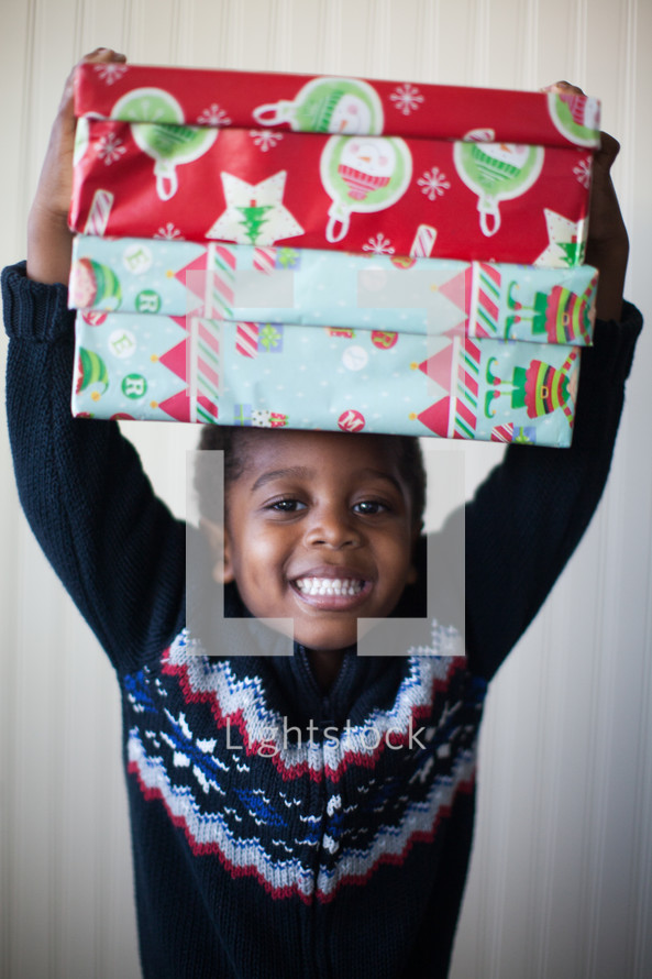 a boy child holding wrapped Christmas gifts over his head 