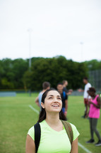 athletes standing on a sports field with backpacks looking up 