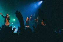 Singers on stage and crowd with arms raised in praise.