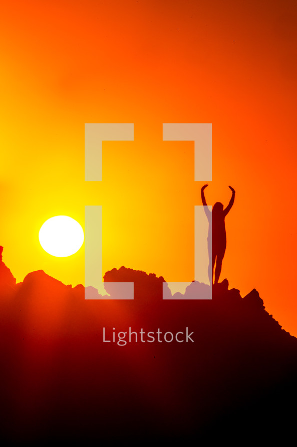 woman standing on a mountain at sunset with raised hands 