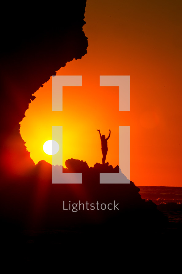 silhouette of a woman standing on a mountain with raised hands at sunset 