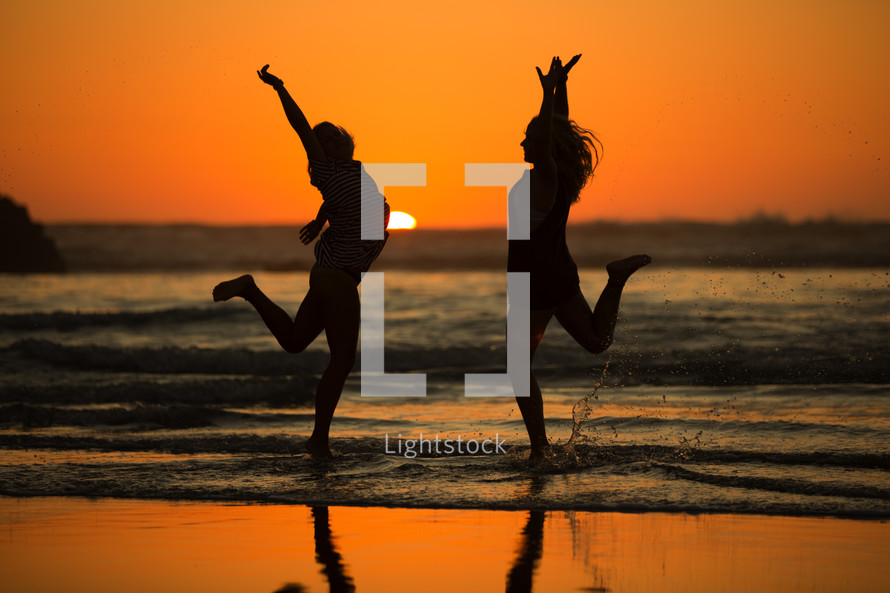 silhouettes of young women dancing on a beach at sunset 