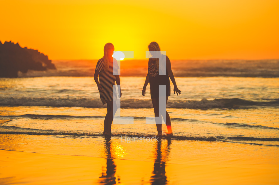 young women walking on a beach at sunset 