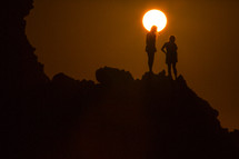 silhouettes of women standing at the edge of a cliff under bright sunlight 