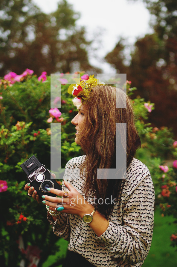 a woman with flowers in her hair holding a vintage camera 