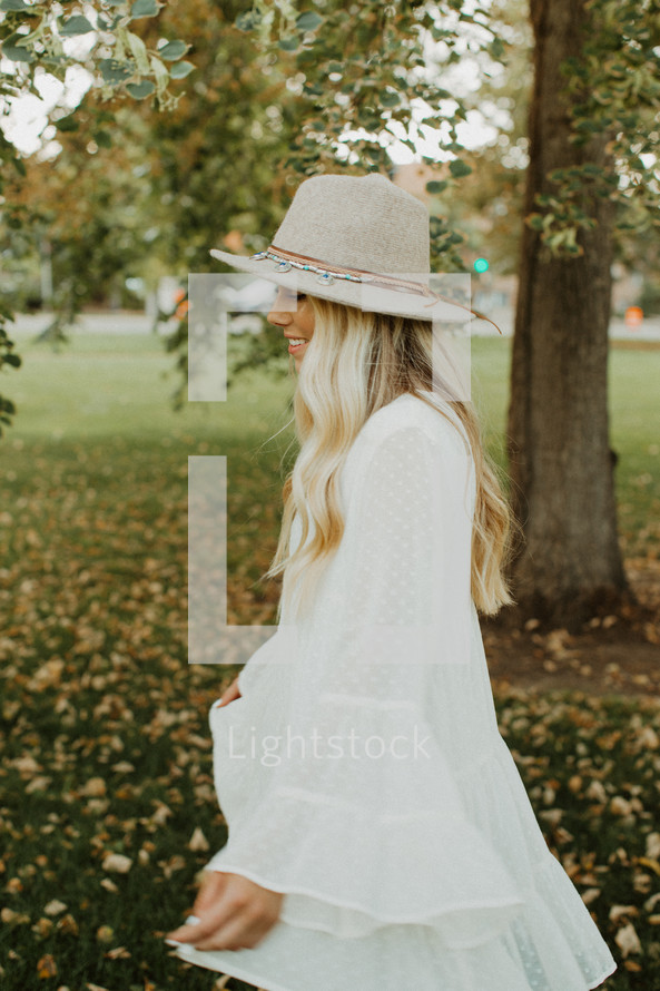 a young woman in a white dress and hat twirling outdoors 