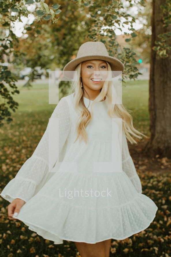 a young woman in a white dress and hat twirling outdoors 