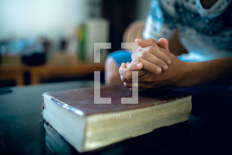 Hands clasped on a Bible praying