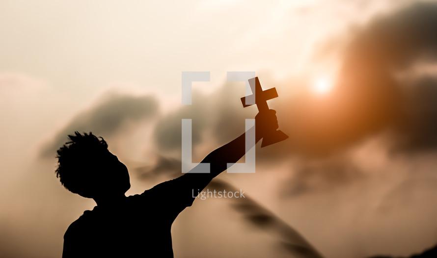 silhouette of a boy holding a cross outdoors 
