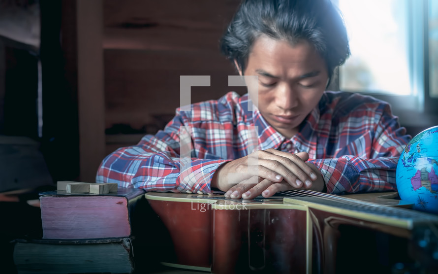 young male praying over a guitar to worship God