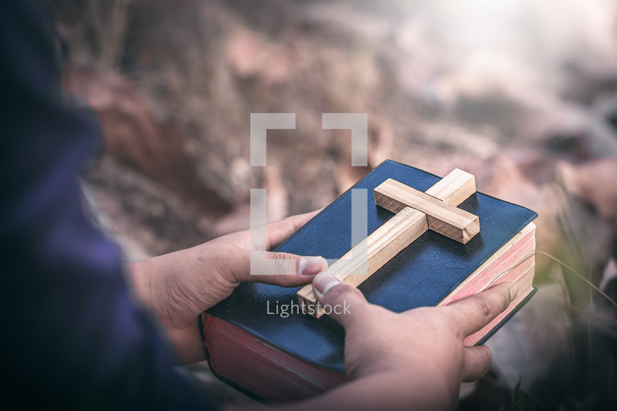 a man holding a wooden cross and Bible outdoors 
