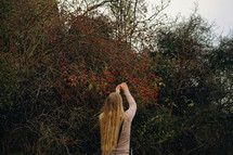 a woman reaching up to touch red berries on a bush