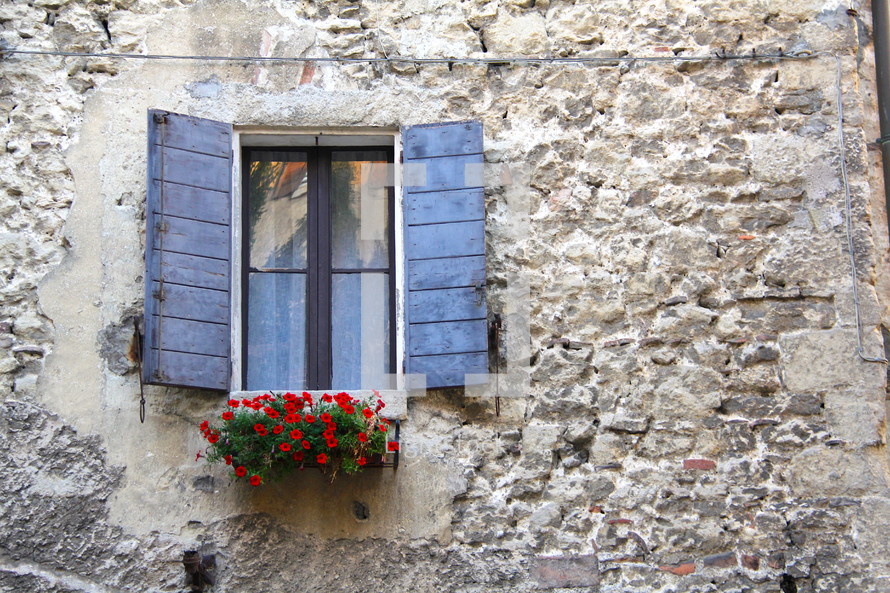 A window box, shutters, and window in a strong stone wall