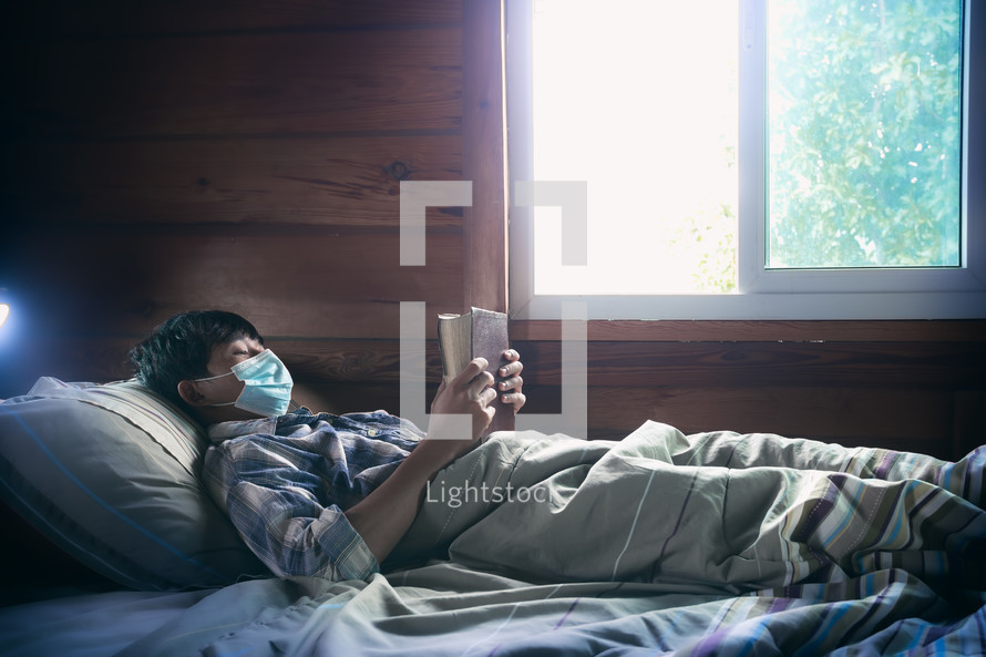 a sick boy lying in bed reading a Bible 