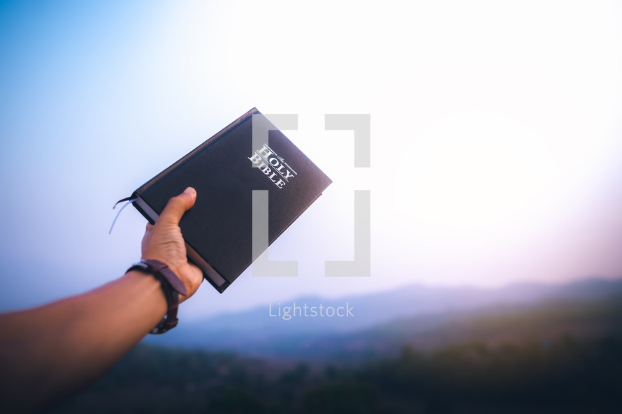 Title: raised hand holding the holy Bible with blue sky in morning. copy space.