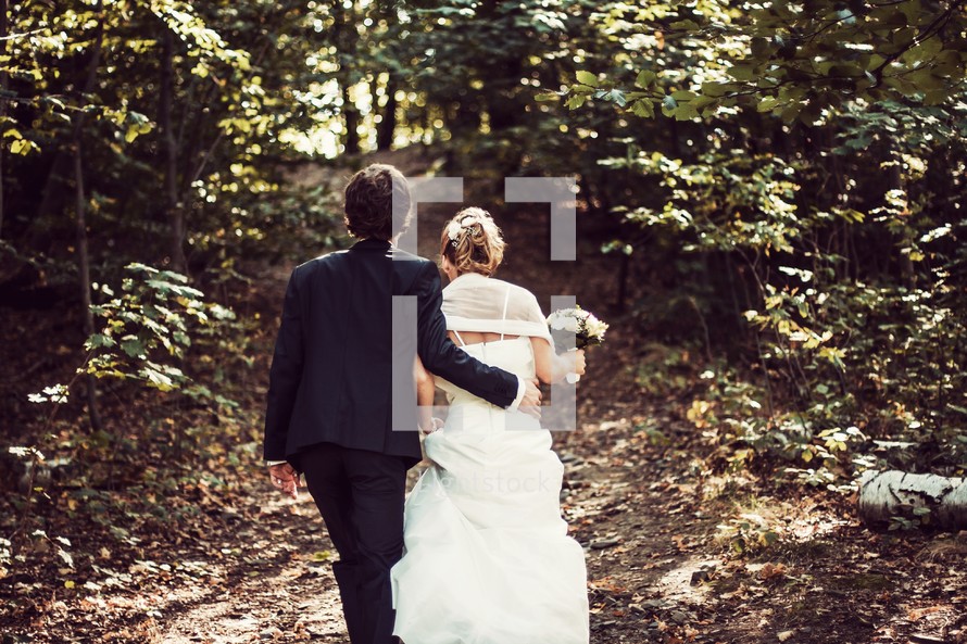 bride and groom walking down a path through a forest 