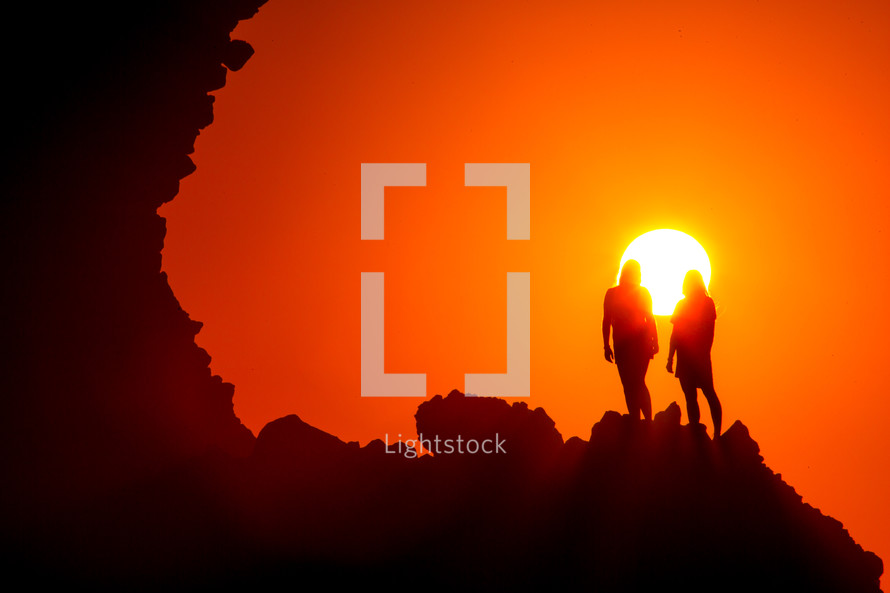 women standing at the edge of a cliff at sunset under a vibrant sky
