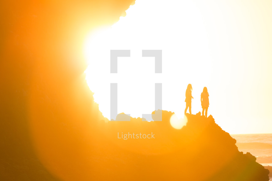 silhouettes of women standing at the edge of a cliff under bright sunlight 