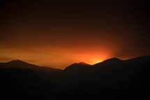 orange glow in the sky as the sun sets behind mountains 
