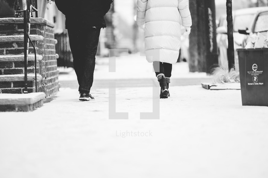 a man and woman walking on a sidewalk in the snow 