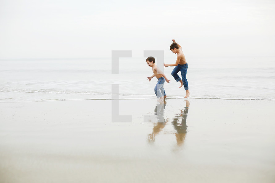 brothers running on a beach in jeans 