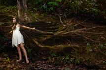 A fairy with wings spread near the roots of a tree.