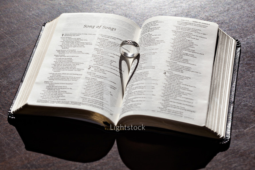 wedding band in the pages of a Bible forming a heart shadow