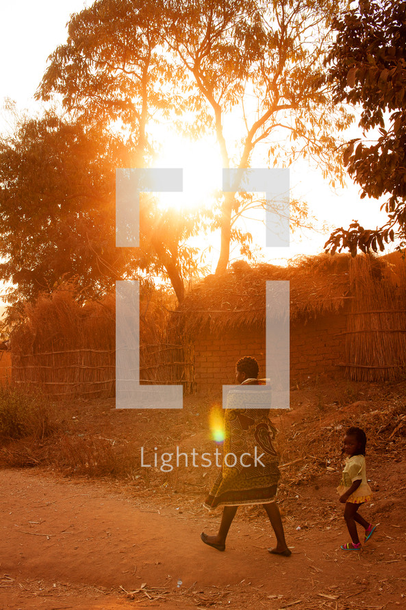 Mother and child walking down a dirt road in Malawi, Africa at sunset. 