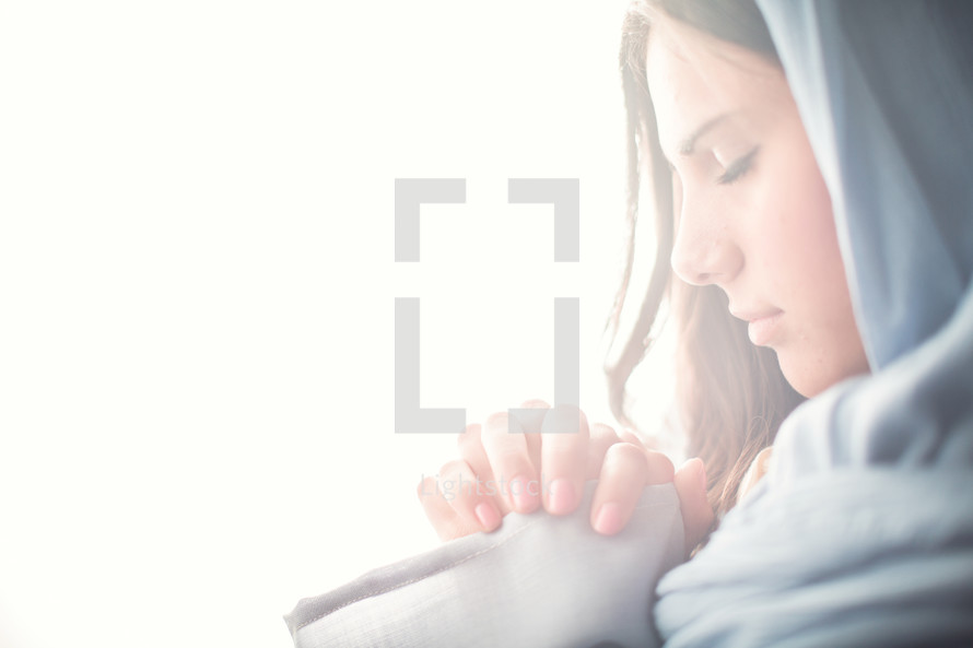 Mary in a blue shroud in bright light with praying hands 