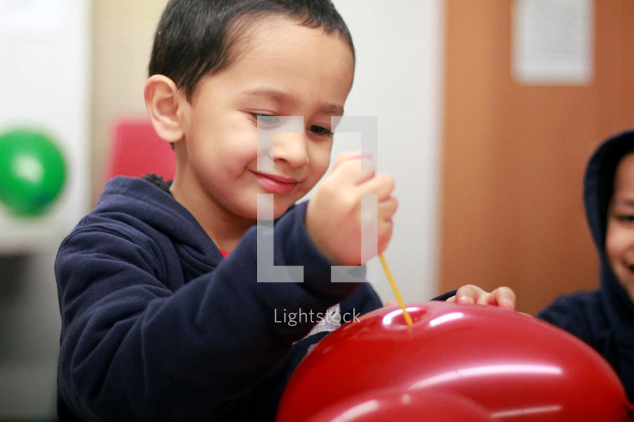 Boy poking a balloon with a straw.