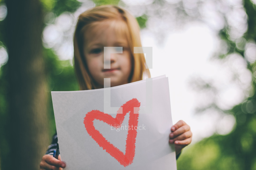 A child holding a sign  with a drawing of a heart.
