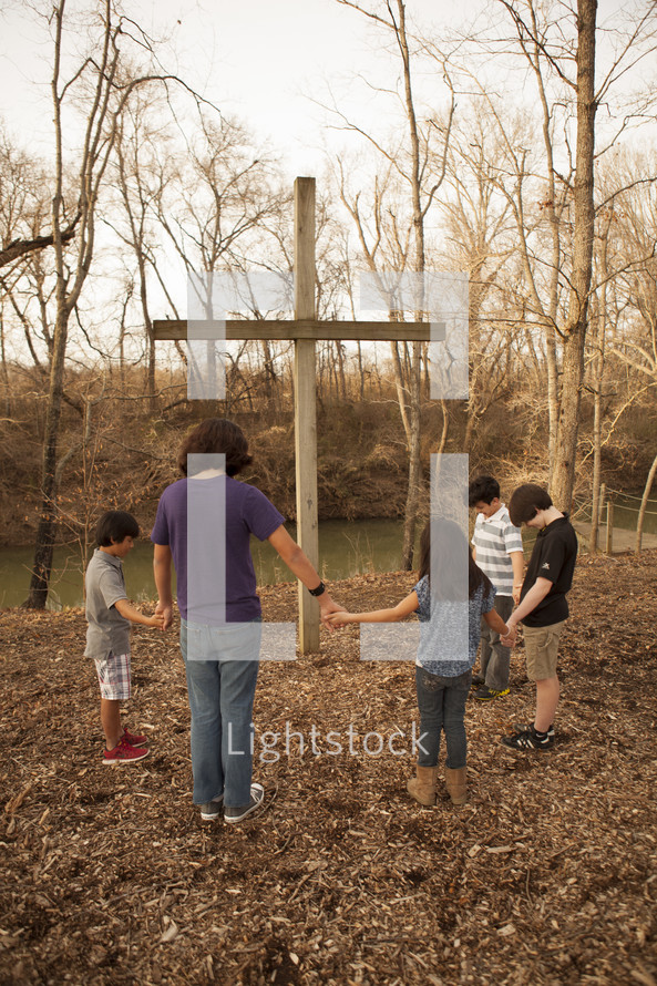 holding hands in prayer in front of a cross outdoors 