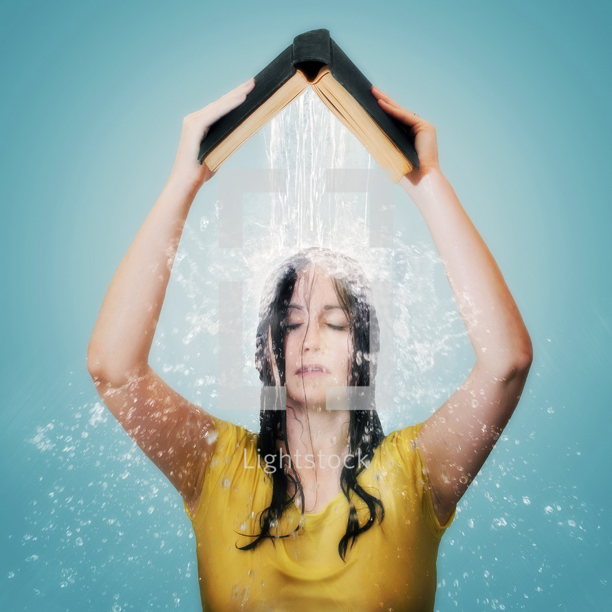 A woman holding an open Bible above her head as water pours on her. 